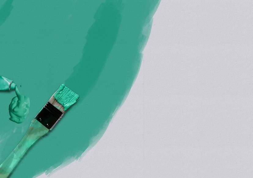 Teal paint tube and brush spread thick turquoise pigment across a textured gray surface in a close-up view.