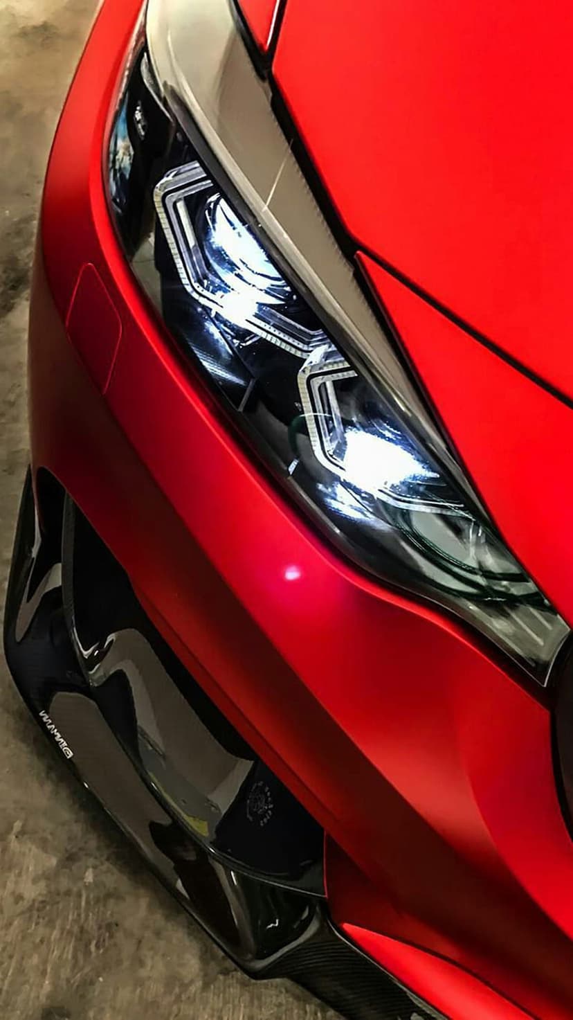 Red Honda Civic headlight with glowing LED accents and a black carbon fiber aerodynamic front splitter.