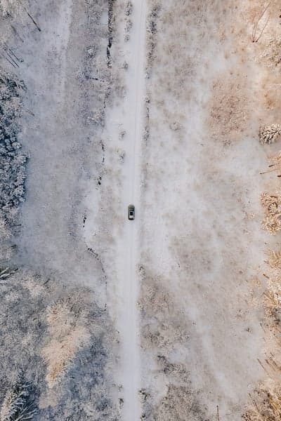 Drone view of car driving on snowy forest road