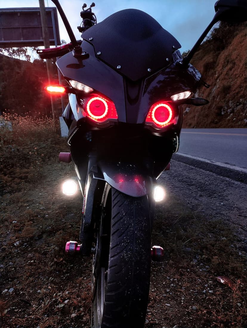 Black sportbike with glowing red halo headlights parked on a roadside under a dark blue twilight sky at dusk.