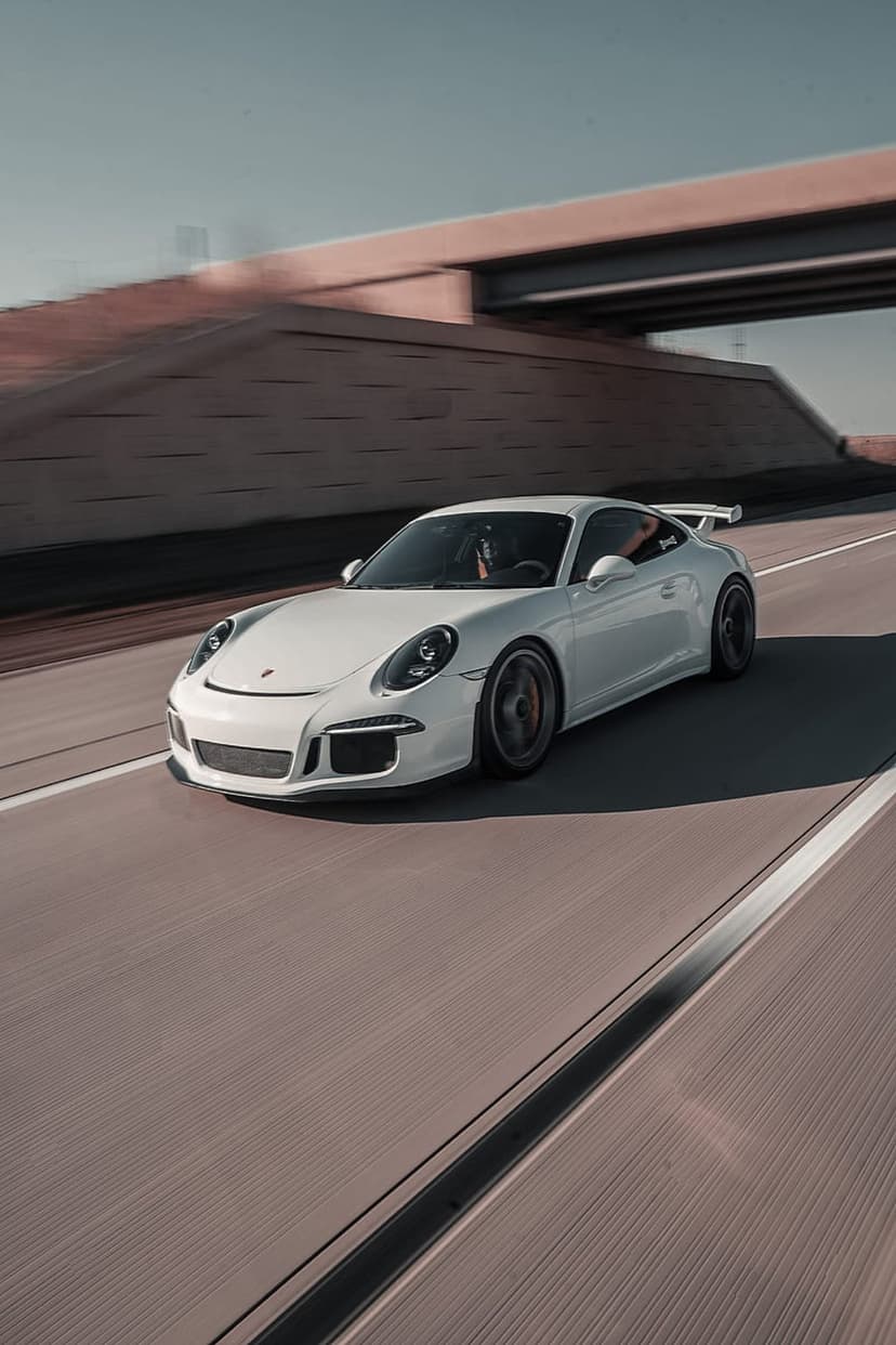 White Porsche 911 GT3 driving on a highway at sunset with motion blur under a concrete bridge.