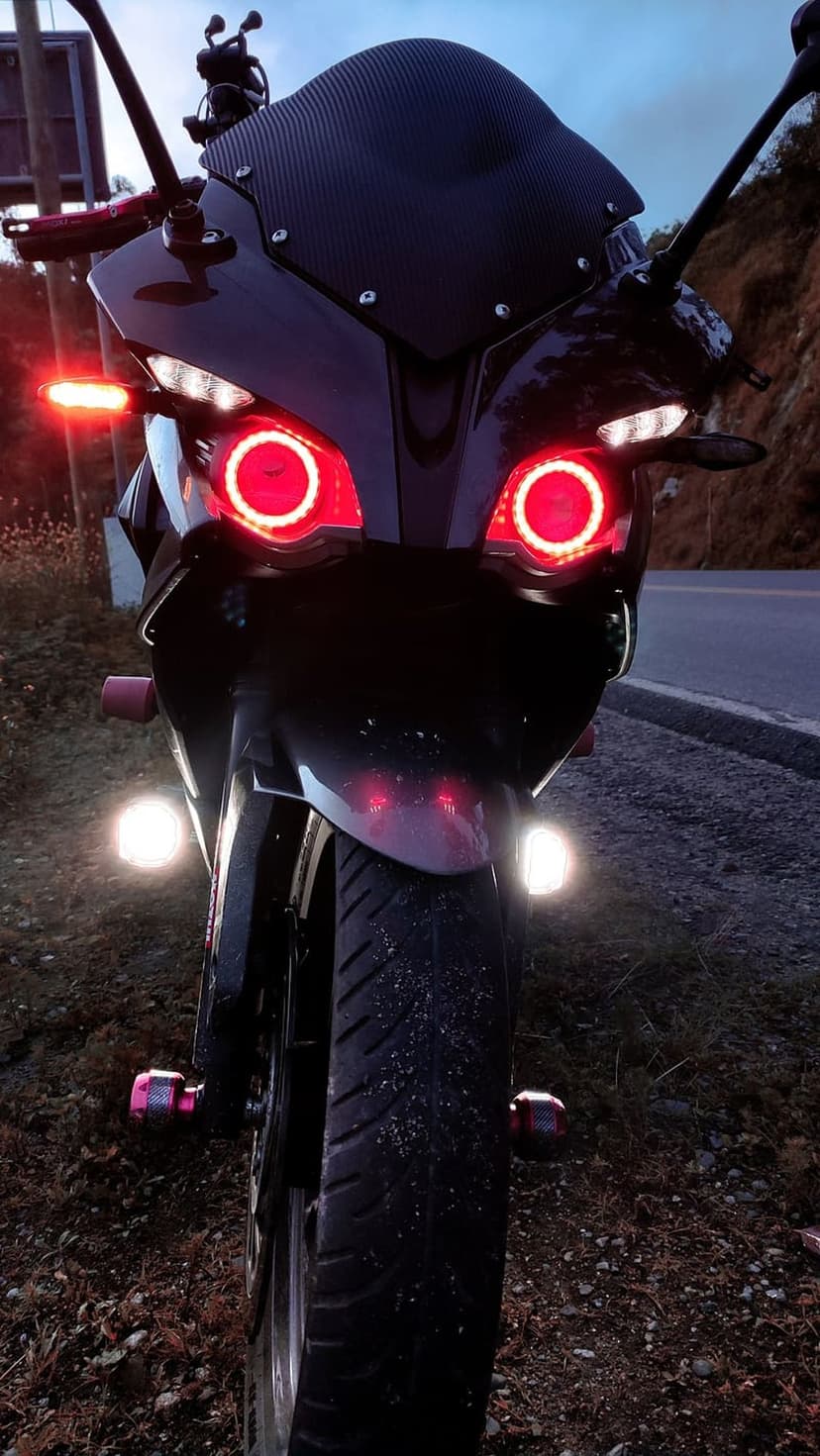 Black sportbike with glowing red halo headlights and white auxiliary lights parked on a road at twilight.