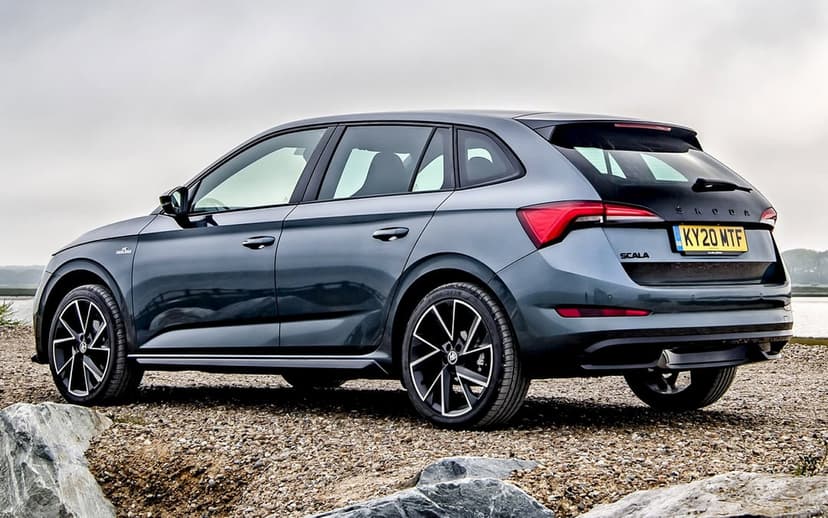 Gray Skoda Scala hatchback parked on a gravel beach with black alloy wheels under a soft misty sky.