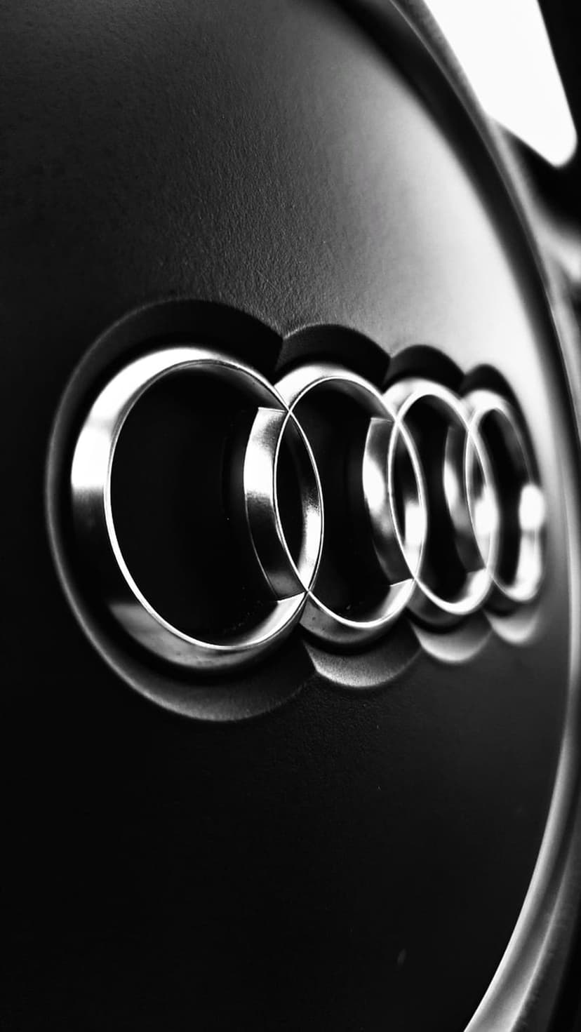 Audi rings in polished silver interlock against a dark background with sharp highlights and soft shadows.