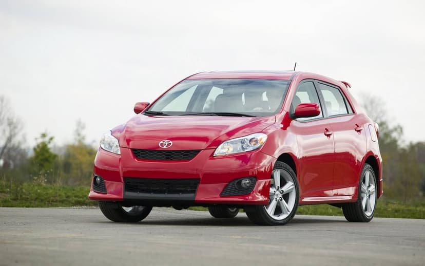 Red Toyota Matrix hatchback parked on a paved road with blurred trees and a pale sky in the background.