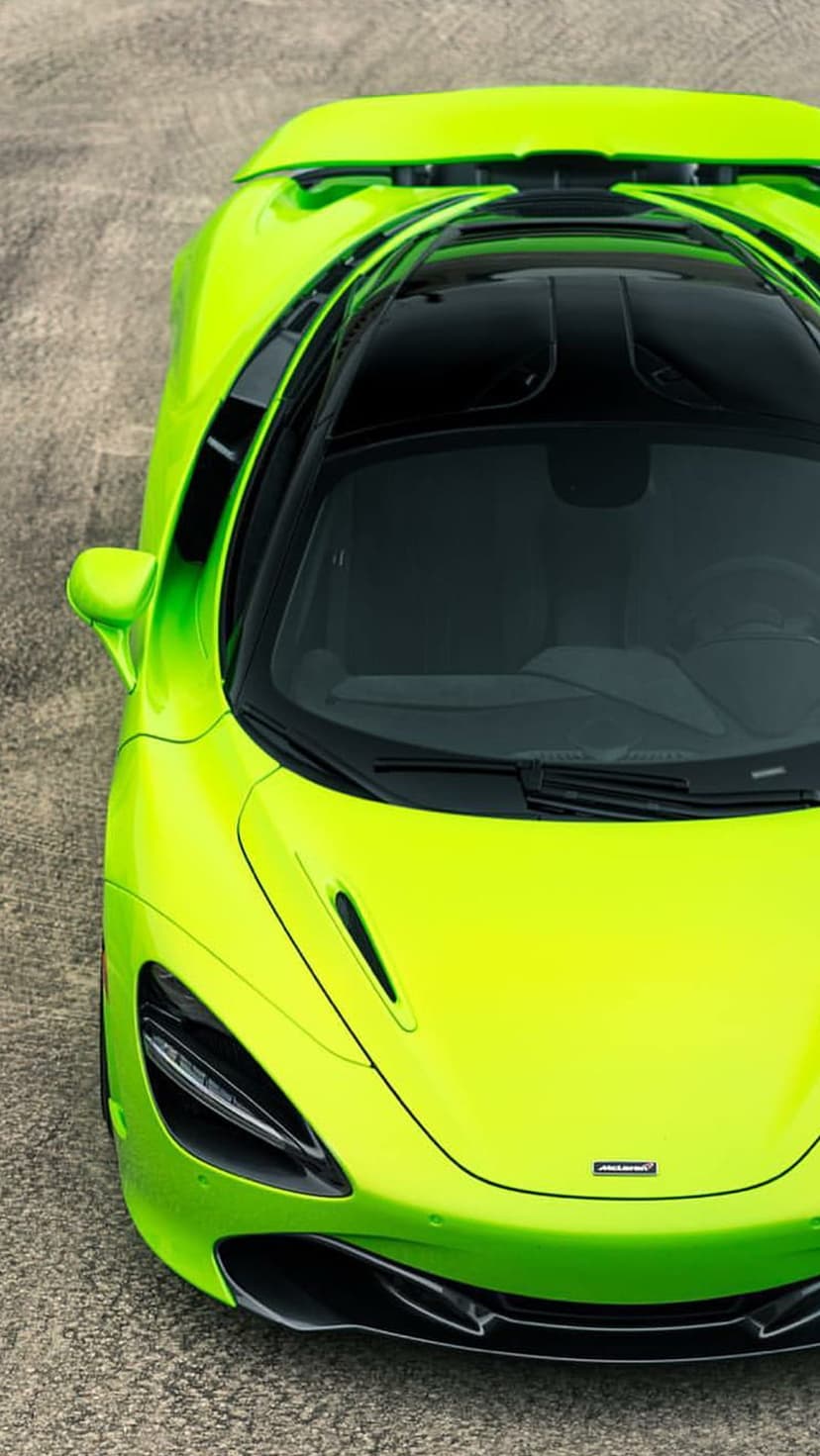 Lime green McLaren supercar seen from above showing its black glass roof on a grey textured road surface.