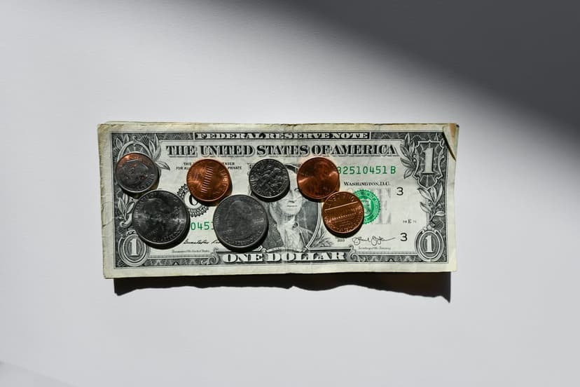 US dollar bill with pennies, quarters, and dimes scattered across its surface on a plain white background.