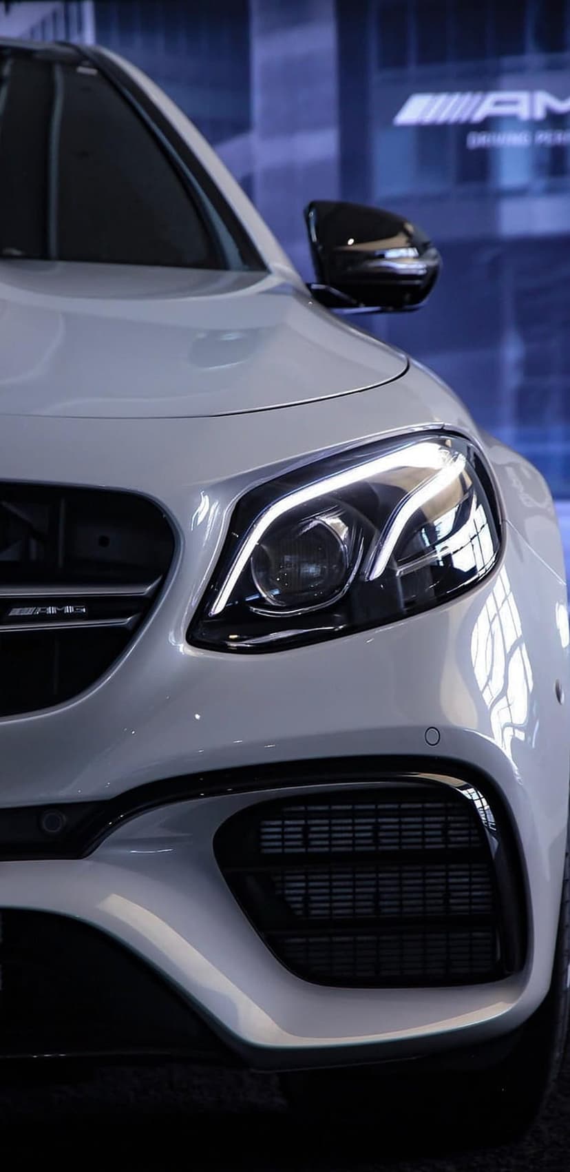 White Mercedes-AMG headlight with sharp LED accents and dark honeycomb grille mesh in a vertical close-up shot.
