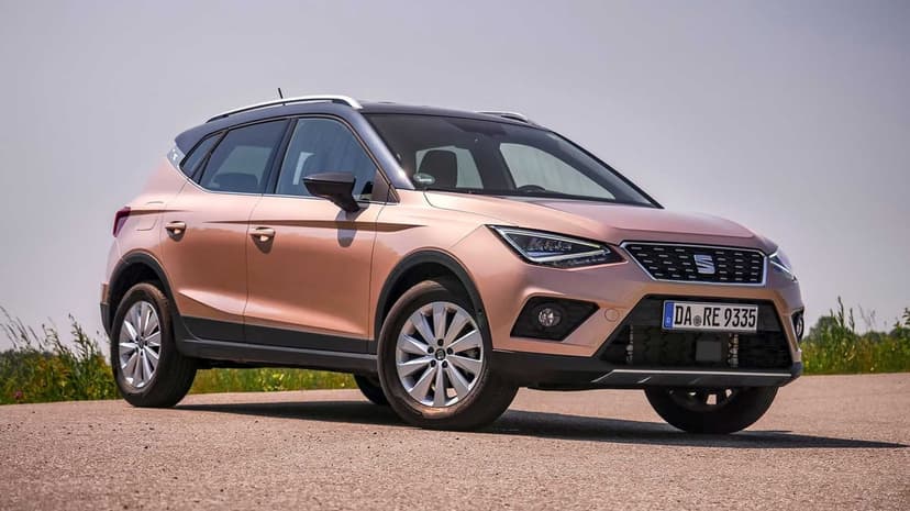 SEAT Arona SUV in rose gold parked on a road with a clear sky background and silver multi-spoke wheels.
