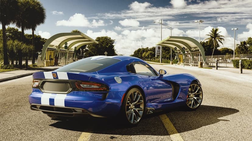 Blue Dodge Viper GTS with white racing stripes parked on a sunny road with palm trees and bus shelters.