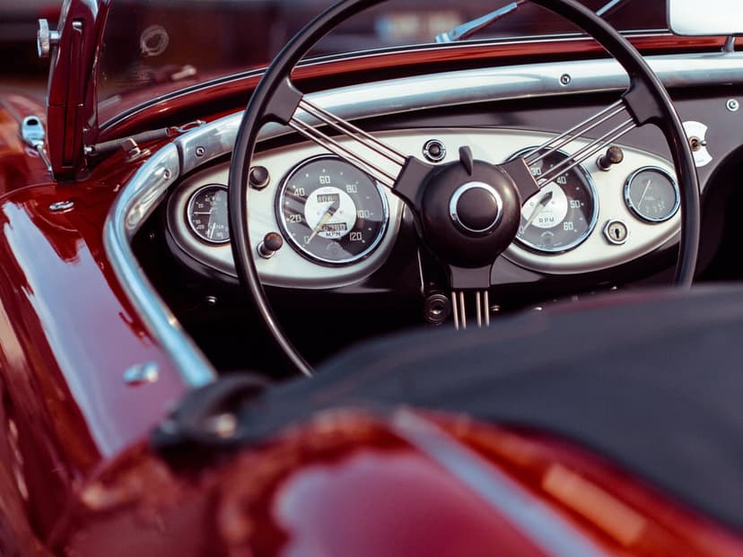 Classic red car cockpit showcasing detailed analog gauges, polished metal trim, and a vintage steering wheel.