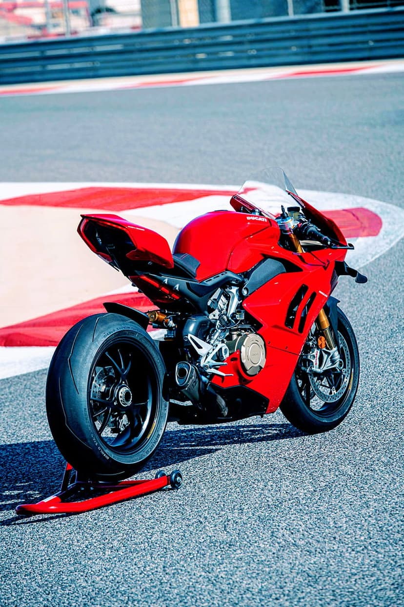 Red Ducati superbike on a paddock stand rests beside vibrantly painted track curbs on a sunlit racing circuit.