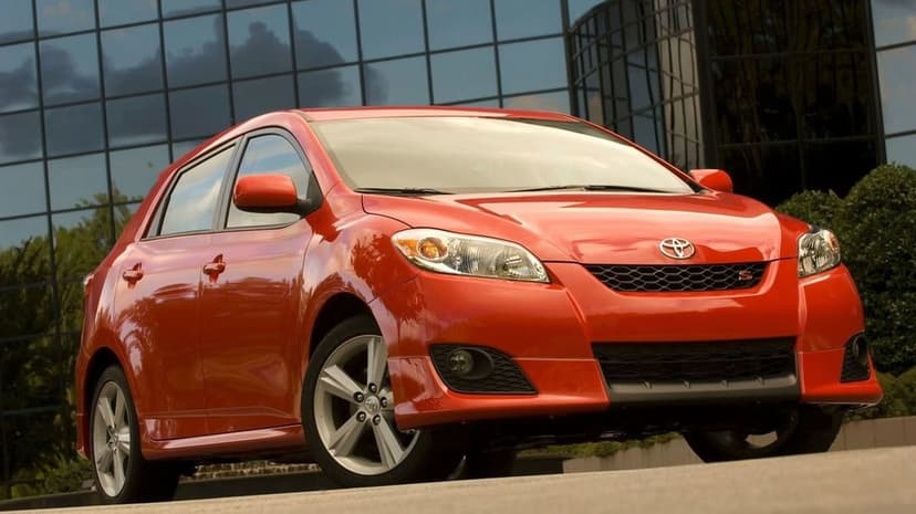 Red Toyota Matrix S hatchback parked in front of a modern glass building with silver wheels and a sporty body kit.