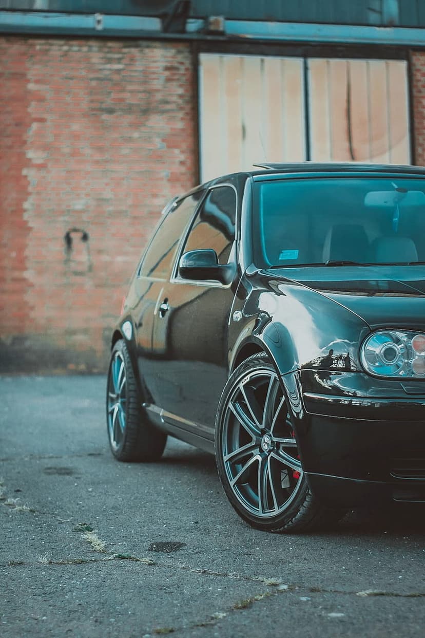 Black Volkswagen Golf GTI with custom wheels parked near a weathered brick wall in a low-angle street shot.