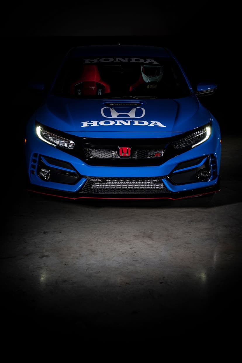 Front view of a blue Honda Civic Type R with white racing decals, red interior seats, and glowing LED headlights.