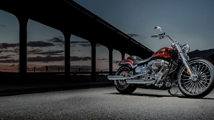Custom orange motorcycle with chrome details parked under massive dark concrete bridge arches at sunset.