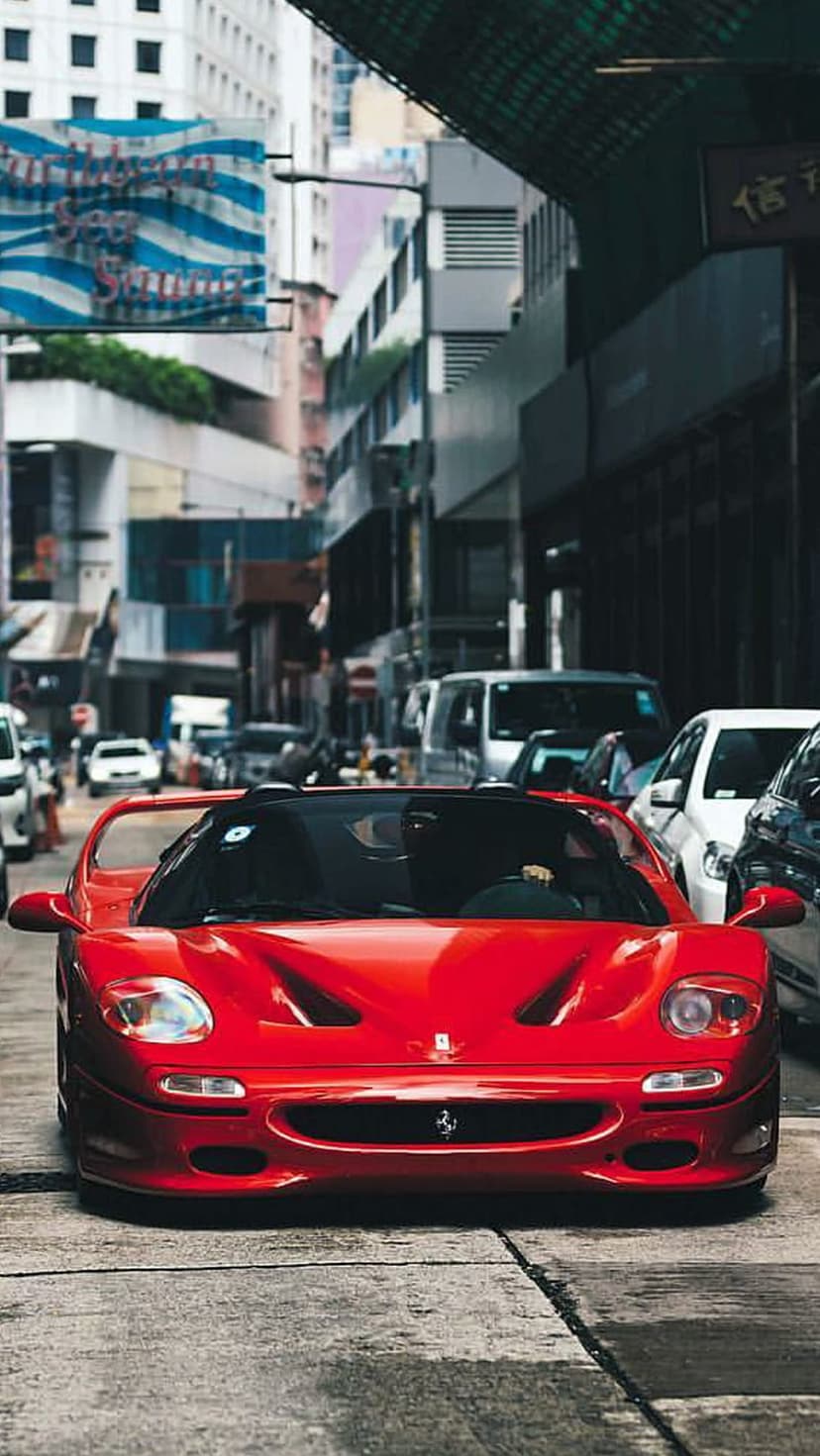 Red Ferrari F50 convertible parked on a weathered urban street with Asian building signs and a bridge background.