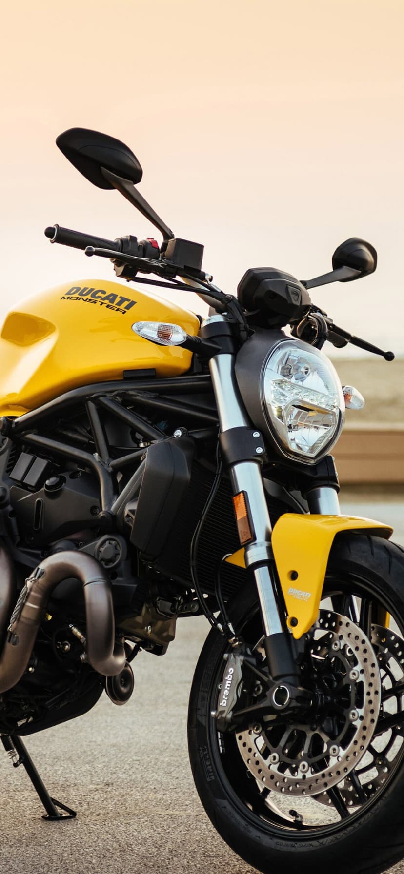 Yellow Ducati Monster motorcycle with black trellis frame and silver forks against a soft light background.