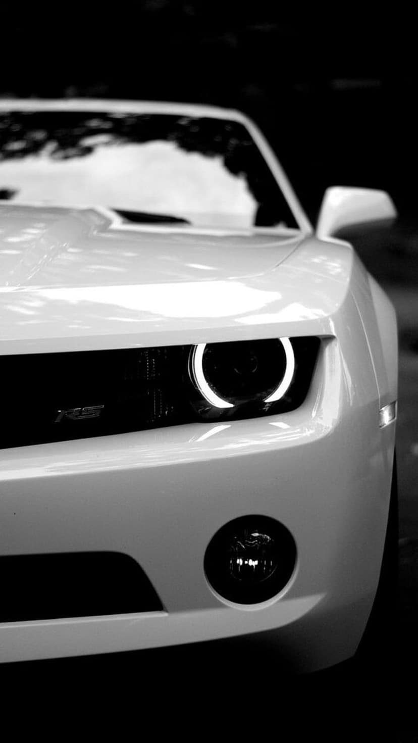 Chevrolet Camaro RS headlight with glowing halo ring and RS badge in a high-contrast black and white close-up.