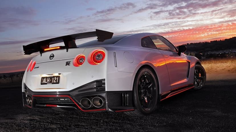 Rear view of a silver Nissan GT-R Nismo with red accents and a large wing under a colorful sunset sky.