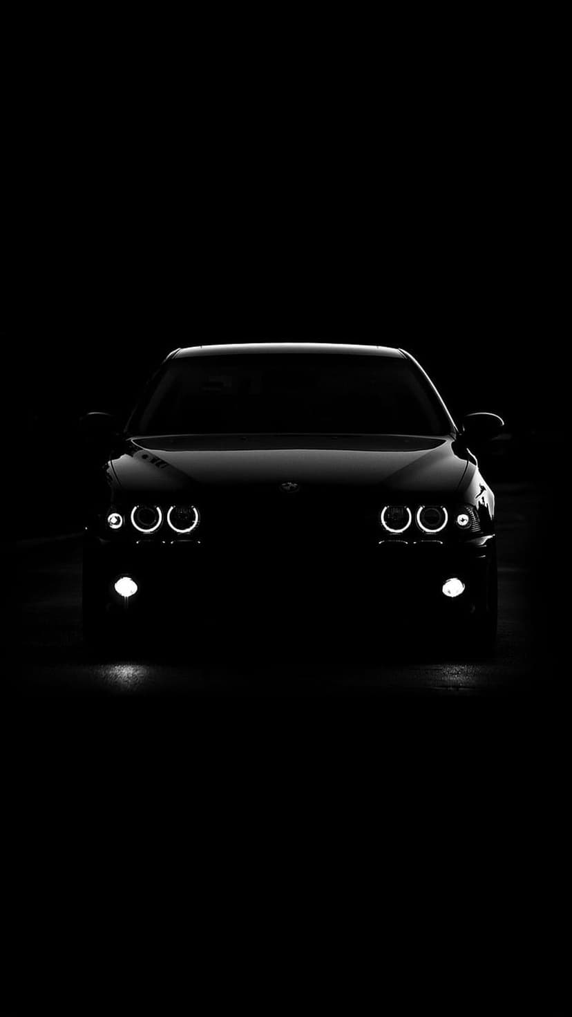 BMW car headlights and fog lights glowing against a pitch black background in a vertical high-contrast shot.