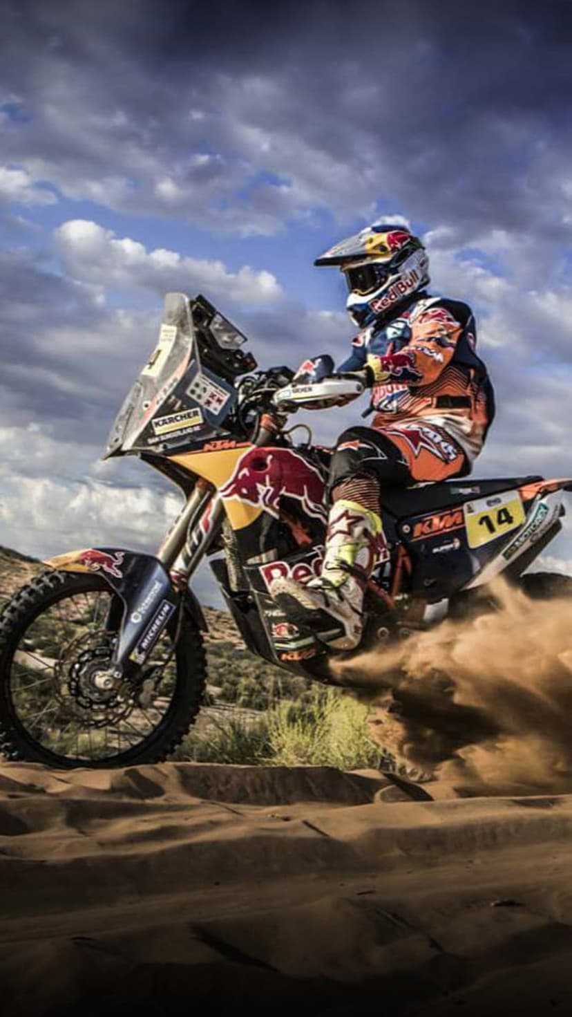 KTM rally motorcycle racer kicking up a massive plume of desert sand under a dramatic and cloudy sky.