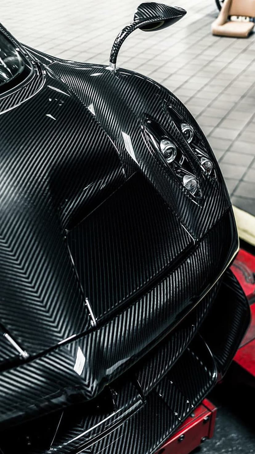 Carbon fiber supercar front fascia with multi-element LED headlights and visible weave texture in close-up view.