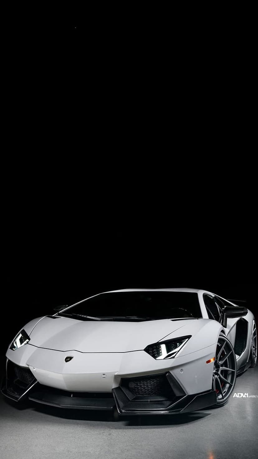 White Lamborghini Aventador front end with glowing headlights and custom wheels against a black background.