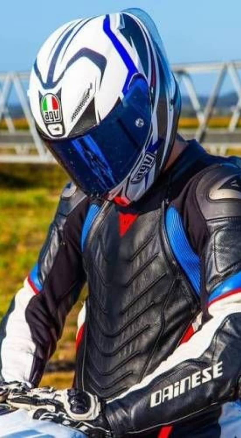 Motorcyclist in a white and blue AGV helmet and black Dainese leather suit looking down at a racing track.