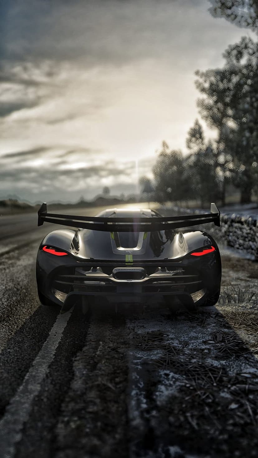 Rear of a dark sports car with red taillights glowing on a wet, muddy rural road during a gloomy dusk setting.
