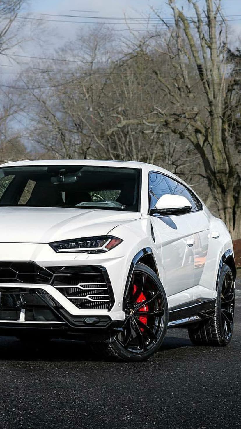 White Lamborghini Urus with black wheels and red calipers on wet asphalt under a cloudy, overcast sky.