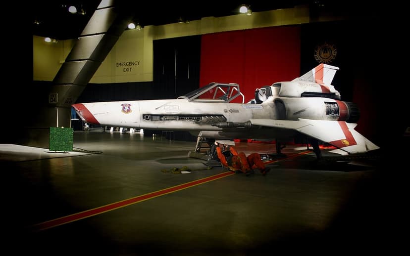 Viper Mk II spacecraft in a dark hangar with a technician in an orange jumpsuit working underneath the hull.