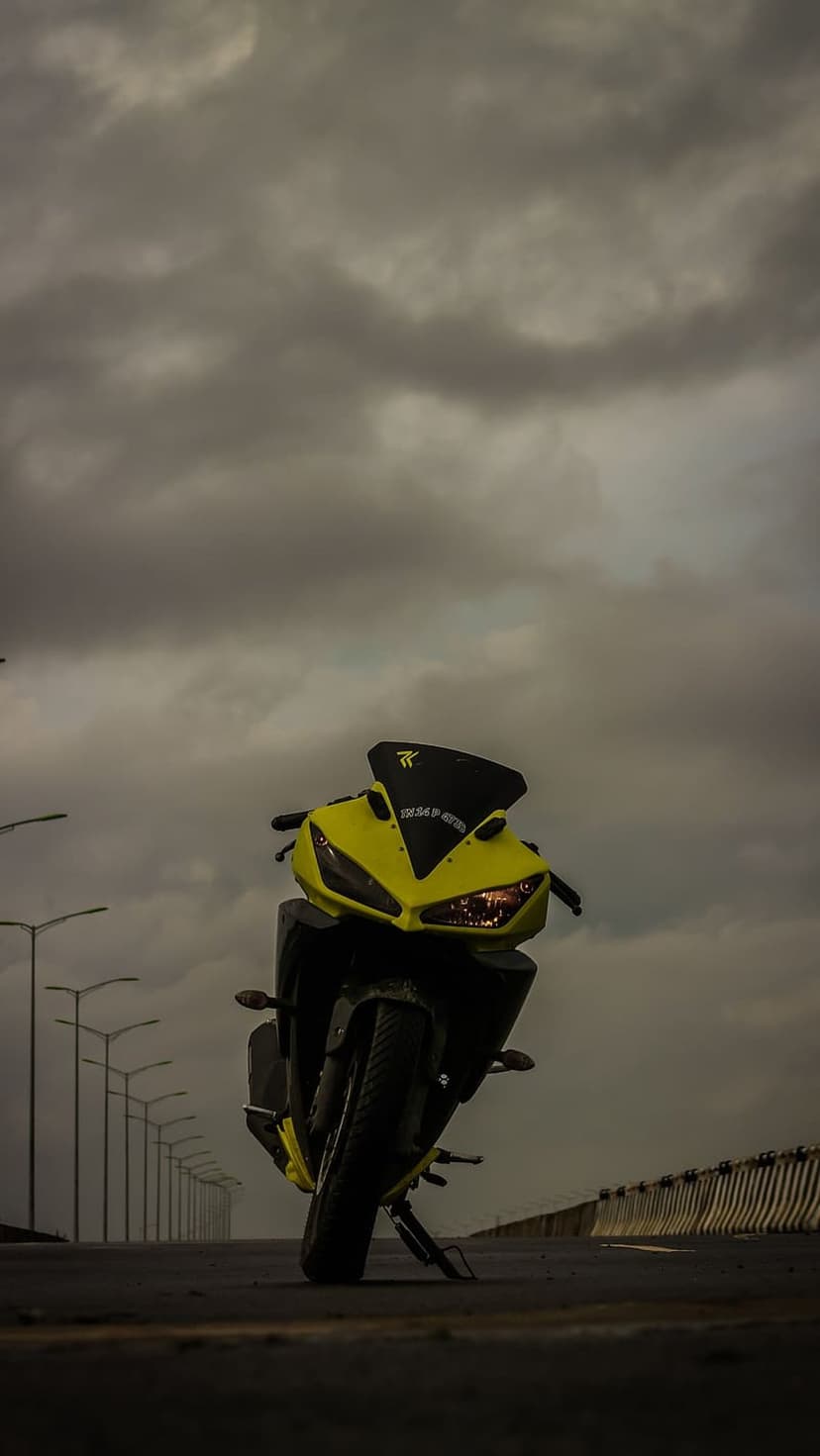 Yellow sports motorcycle with aggressive fairings parked on an asphalt road under a dark overcast sky at dusk.