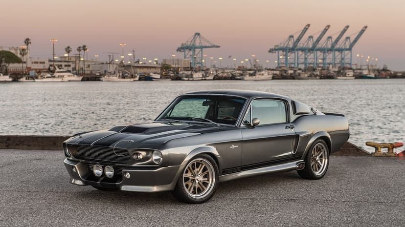 Shelby GT500 Eleanor Mustang parked at a harbor dock with industrial cranes under a soft sunset sky.
