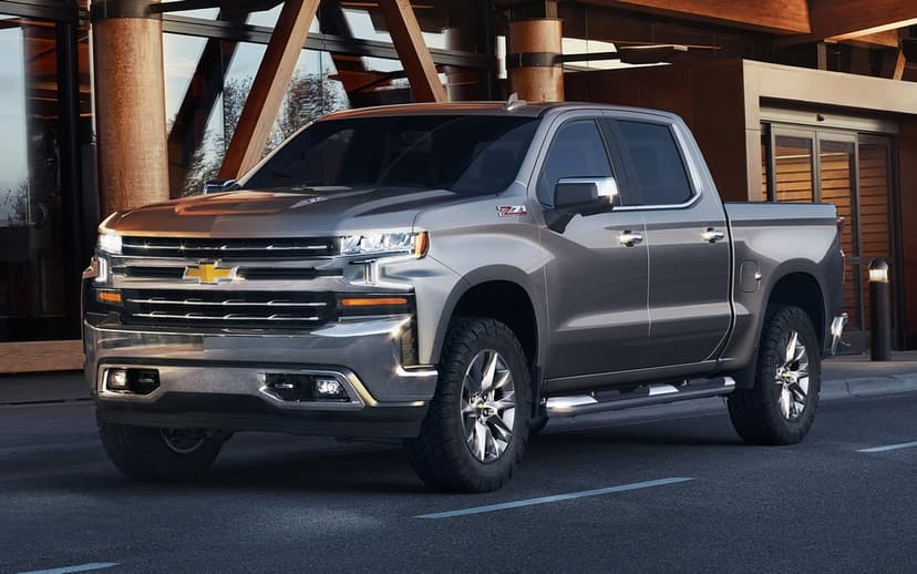 Gray Chevrolet Silverado Z71 pickup truck with chrome accents and LED lights parked by a wooden building.