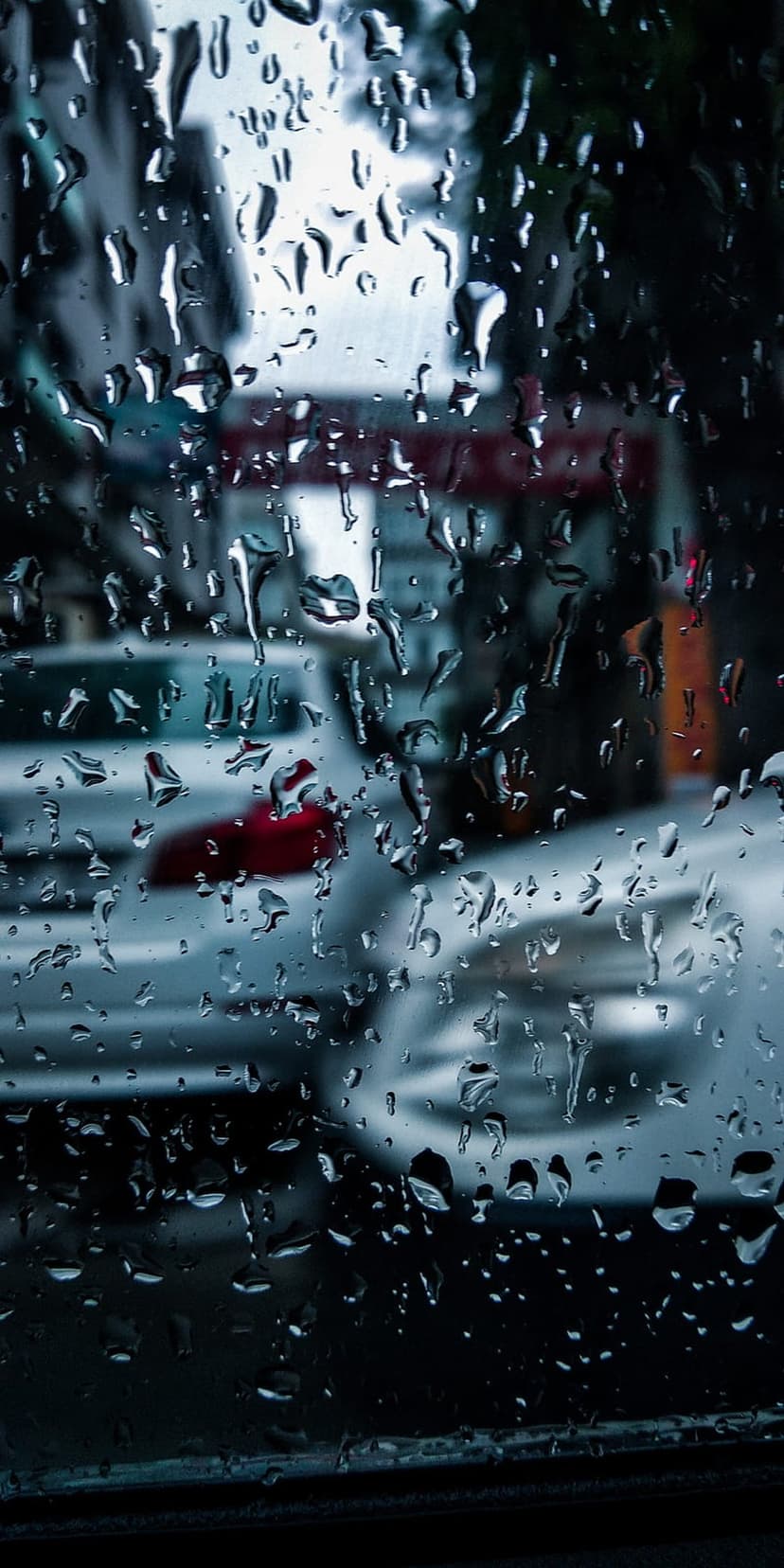 Large water droplets on a transparent window pane overlooking a blurred street with traffic lights in the rain.