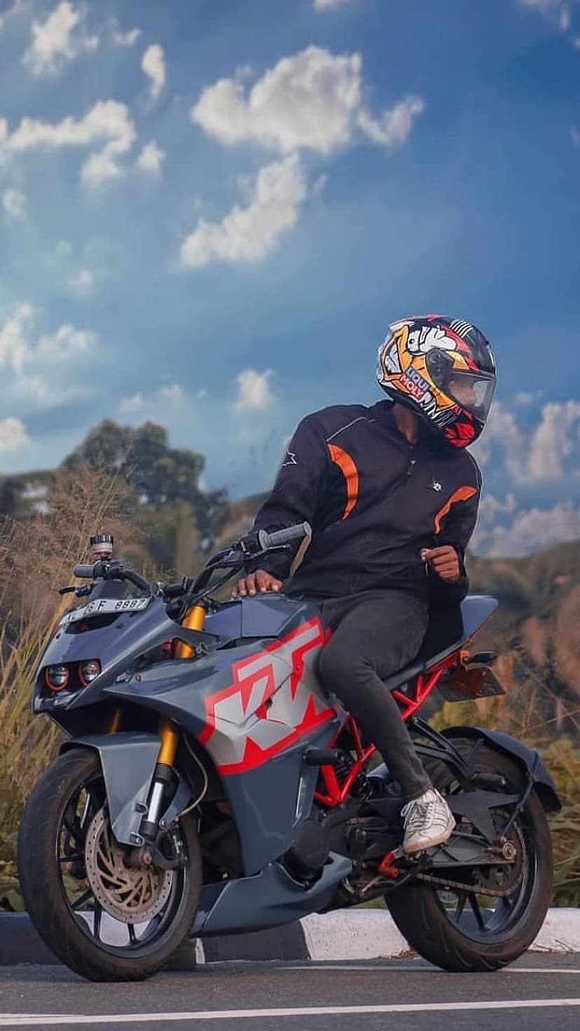 Rider on a gray and red KTM motorcycle wearing a helmet and jacket under a bright blue sky with white clouds.