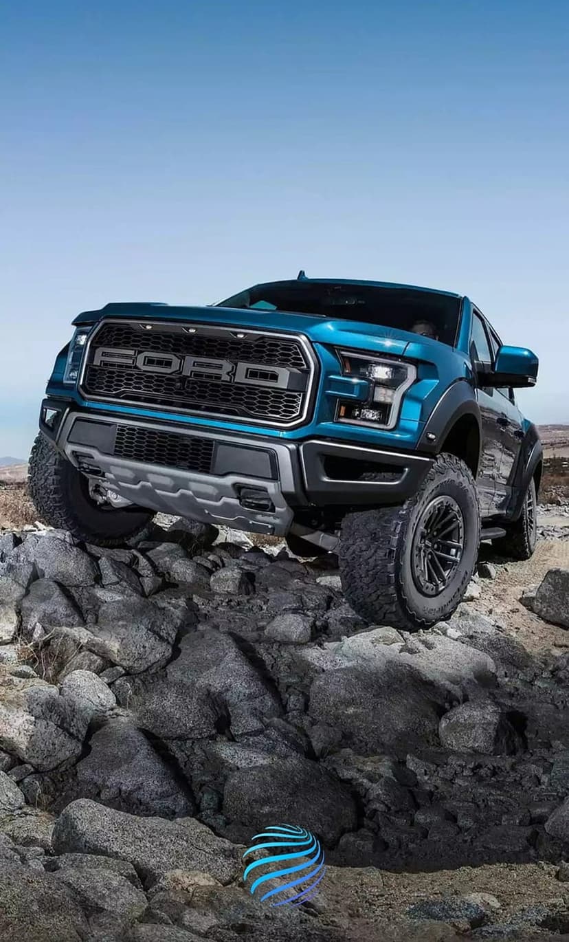 Blue Ford Raptor truck climbing grey boulders under a bright sky on a steep off-road mountain trail.