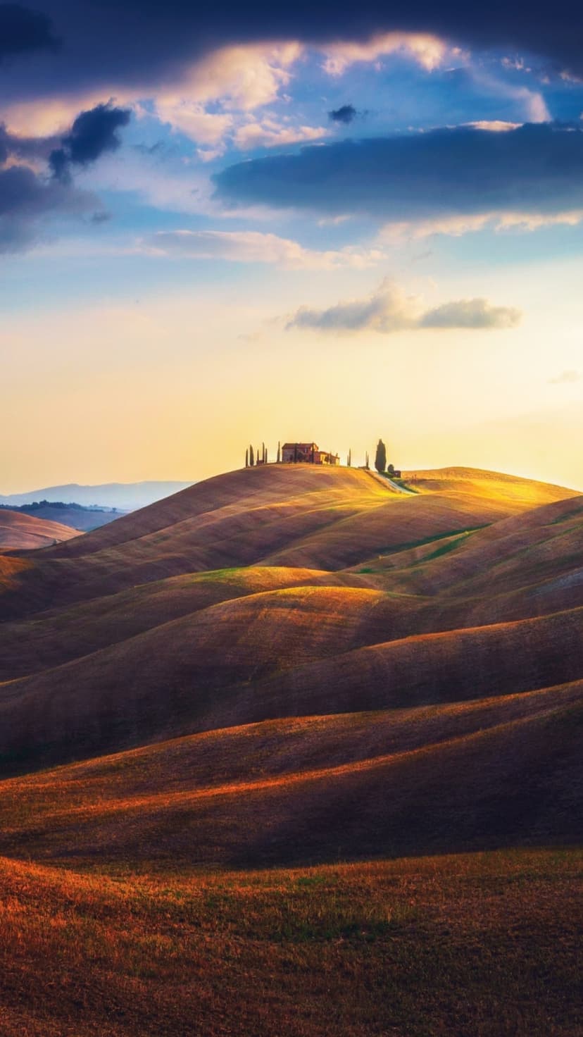 Golden rolling hills of Tuscany with a silhouetted farmhouse and cypress trees under a purple sunset sky.