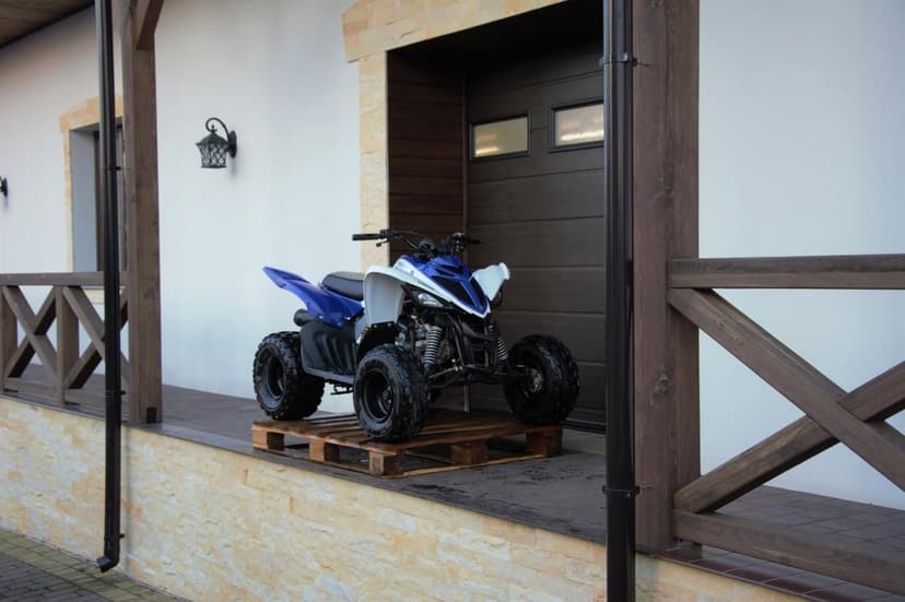 Blue and white Yamaha sport ATV parked on a wooden pallet on a modern terrace with a white wall background.