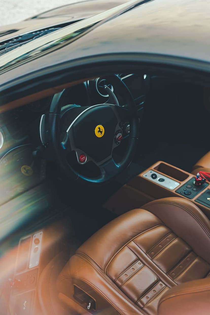 Ferrari steering wheel with prancing horse emblem and tan leather seats inside a luxury supercar cabin.