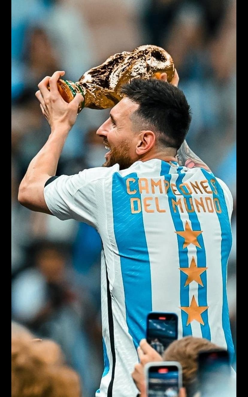 Lionel Messi raises the gold FIFA World Cup trophy wearing a white and blue Argentina jersey among stadium fans.