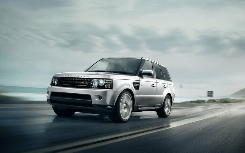 Silver Range Rover Sport driving fast on a wet coastal road under an overcast sky with motion blur.
