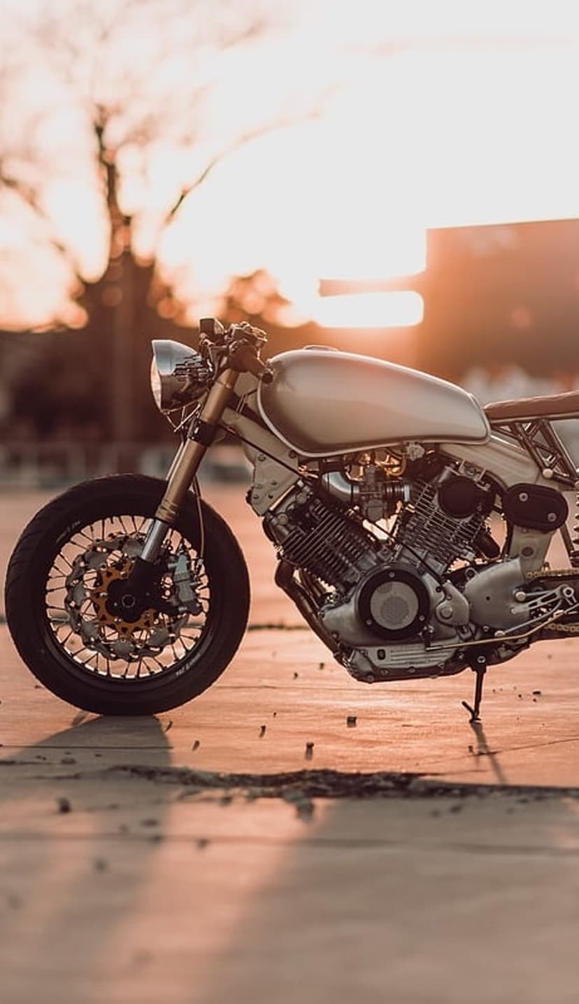 Vintage cafe racer motorcycle gleaming in golden sunset light with detailed chrome parts and blurred background.