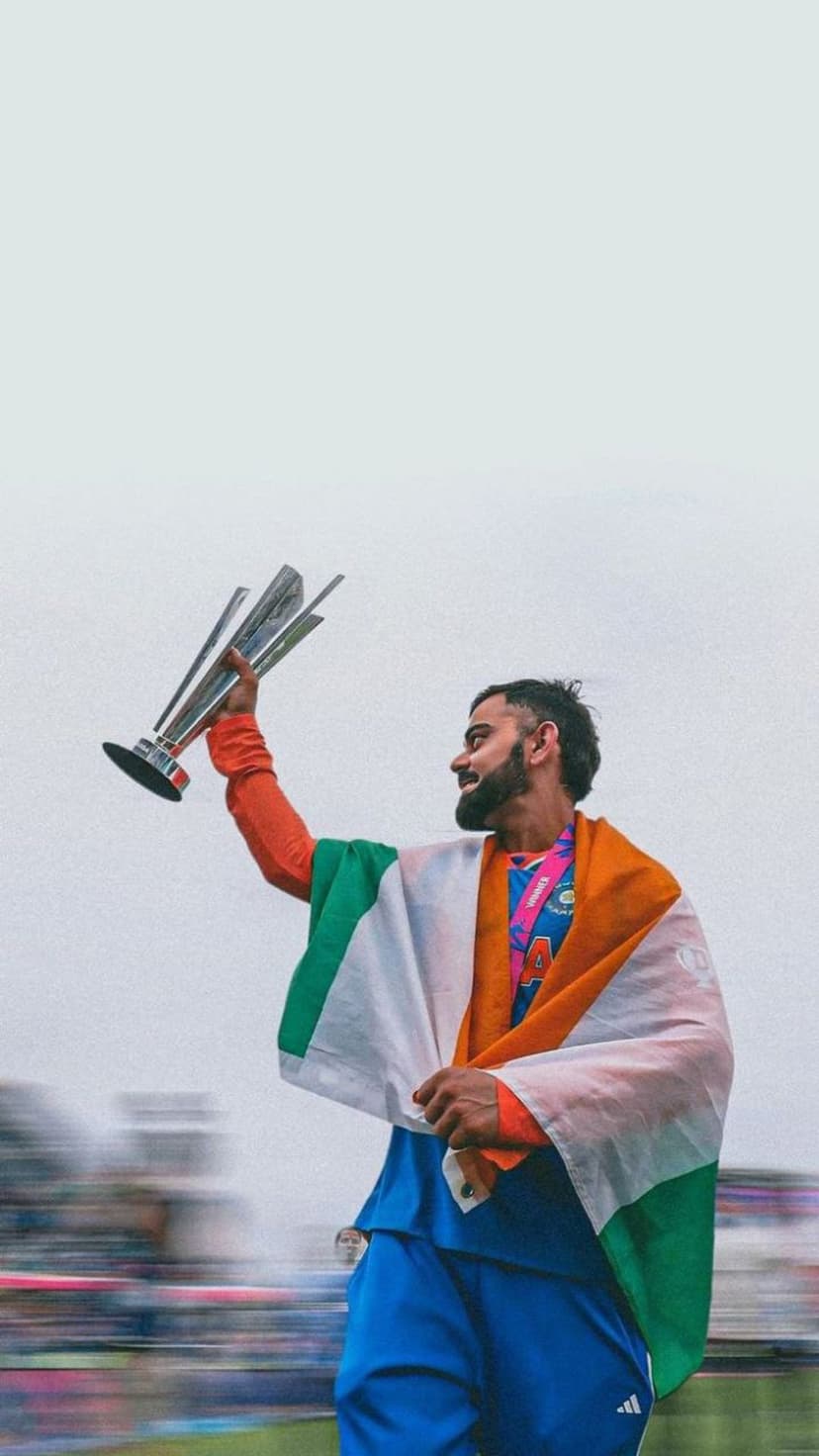 Virat Kohli holds a gold trophy while wearing the Indian flag over his orange jersey in a celebratory stadium.