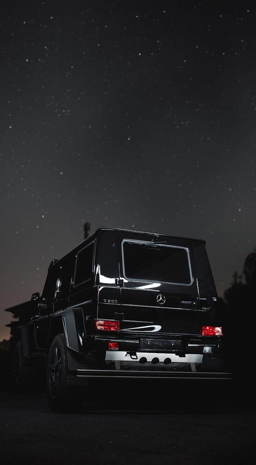 Black Mercedes G-Wagon parked under a dense field of stars in a dark sky with glowing red taillights.