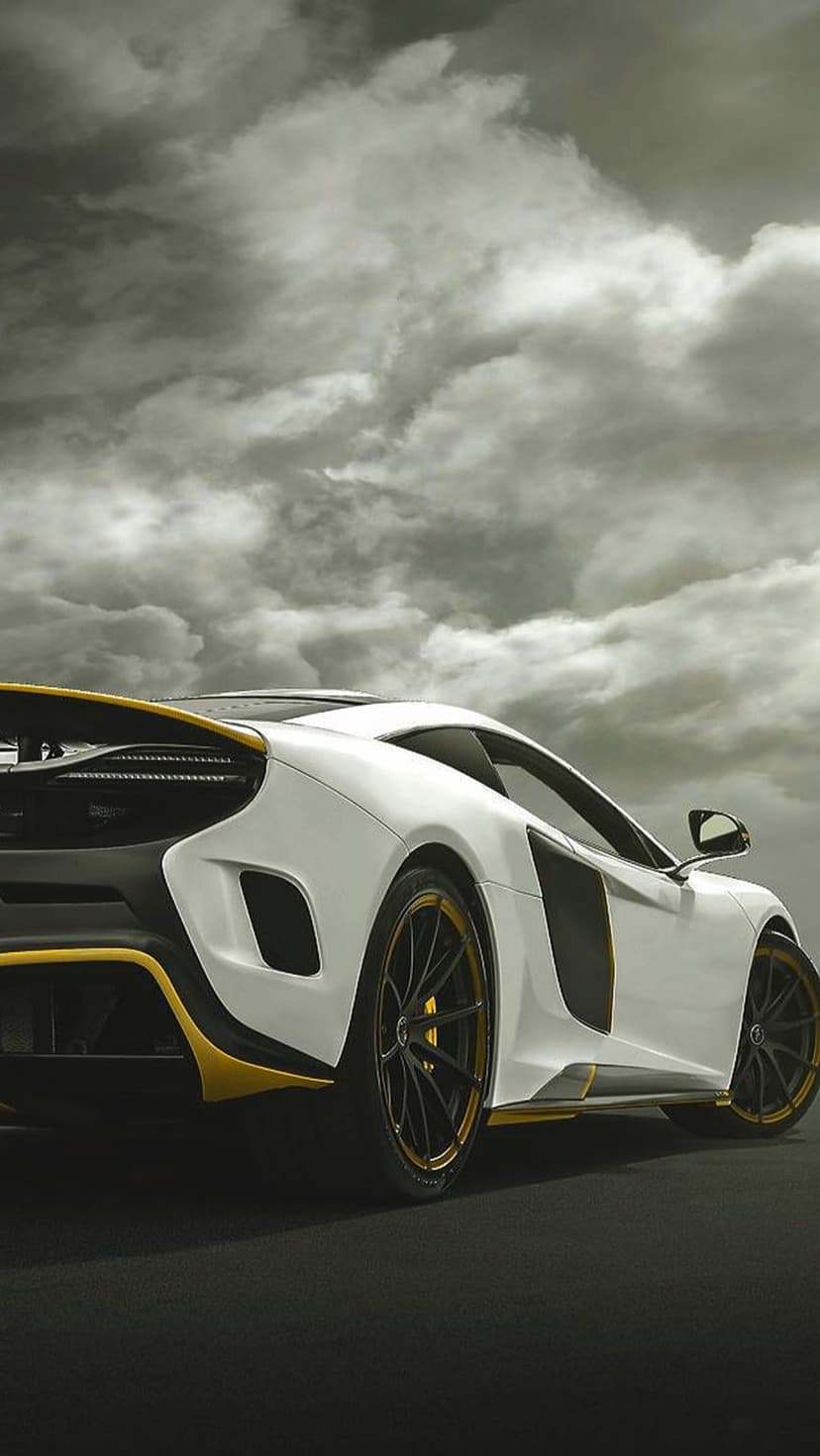White McLaren supercar with yellow accents parked on a dark road under a dramatic grey sky with turbulent clouds.