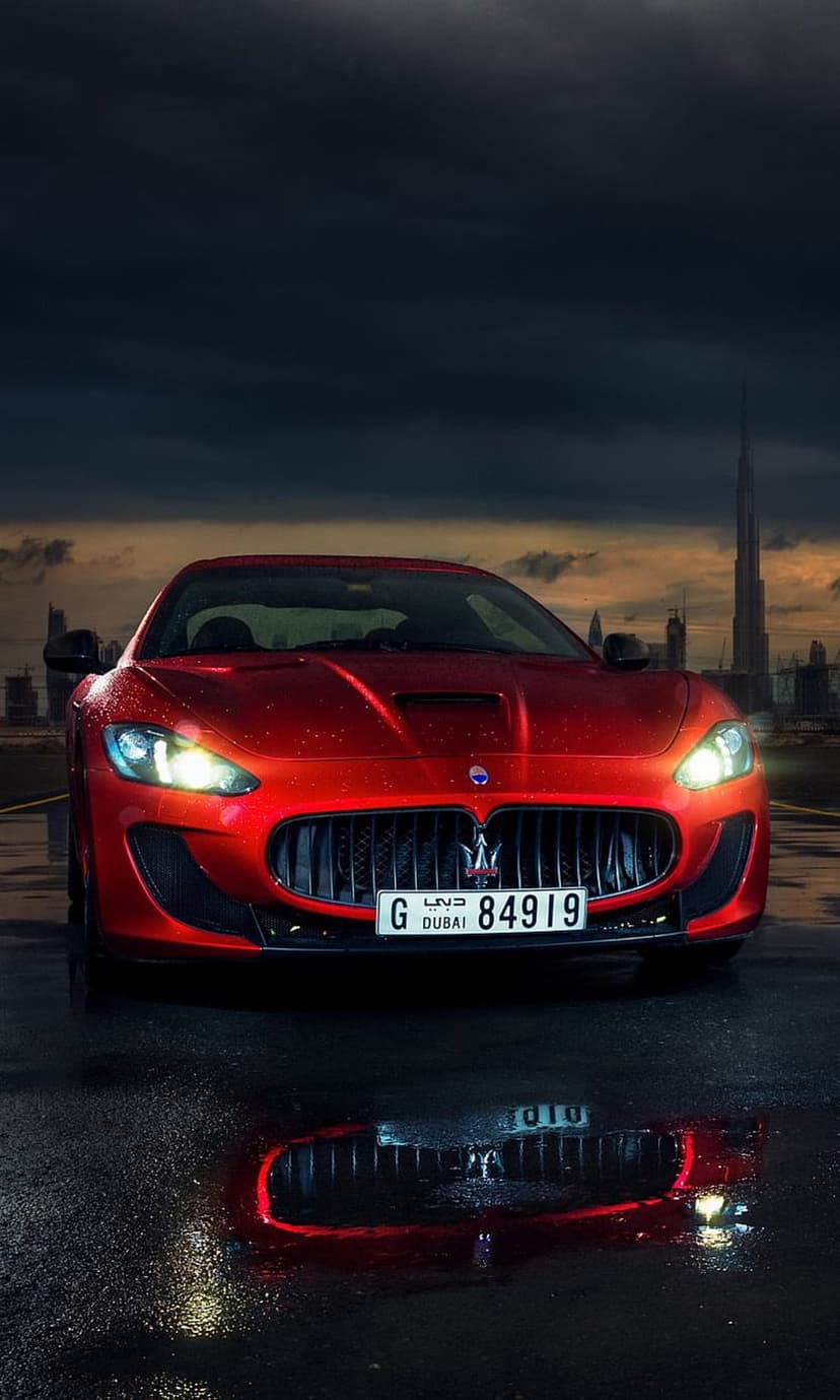 Red Maserati GranTurismo on a wet road with the Burj Khalifa under a cloudy sky during a Dubai evening.