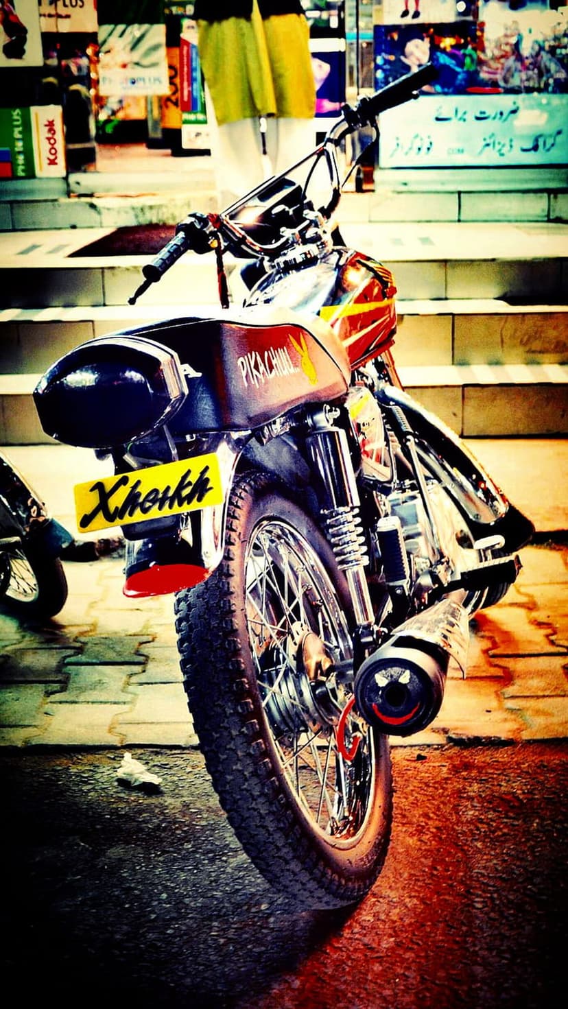 Motorcycle rear seat with a Pikachu logo positioned above a yellow license plate and a rugged spoked knobby tire.