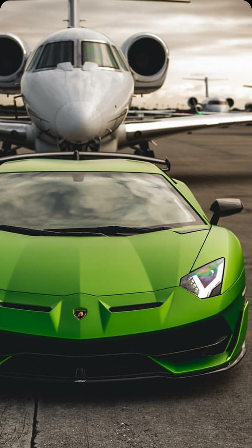 Lime green Lamborghini Aventador parked on a concrete tarmac in front of a silver private jet under a cloudy sky.